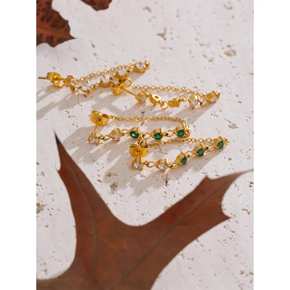 Gold-tone chain bracelets with green and clear stones, everyday jewelry on a light textured surface.